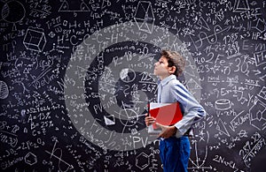 Boy with notebooks against big blackboard with mathematical symbols