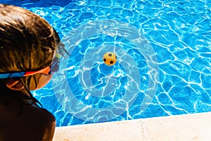 Boy observing a ball moving away from him in a pool in summer, concept of achievable goals in childhood