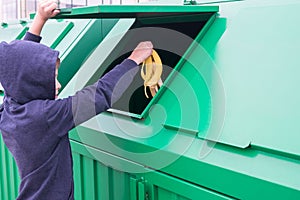 The boy opens the trash tank and throws out a banana skin