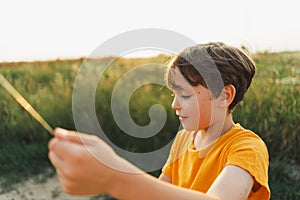A boy in an orange T-shirt flies a kite in nature. Happy child