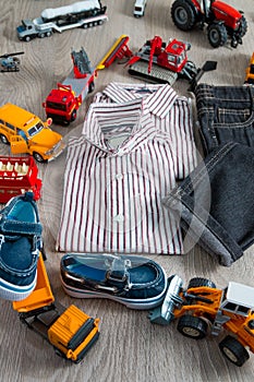 Boy outfit near car toy. Striped shirt, denim pants and blue boat shoes yellow red cars. Top view.