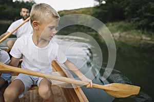 Boy paddling canoe with his dad in background