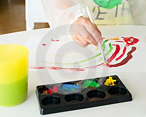 Boy painting with a brush and tempera paint and with a child`s drawing