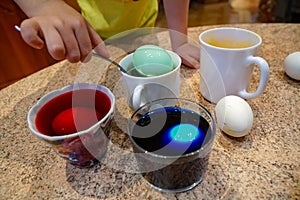 Boy paints eggs for Easter, use spoon dips eggs into colored water in the home interior