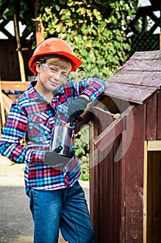 Boy paints the wall of a wooden house. son helps parents with painting the garden house