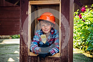 Boy paints the wall of a wooden house. son helps parents with painting the garden house