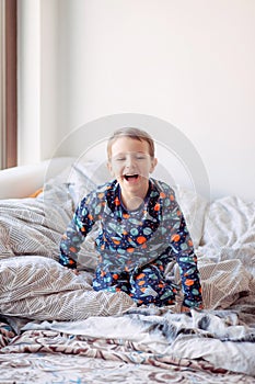 A boy in pajamas with space drawings jumps on the bed, morning exercises of the boy, good morning