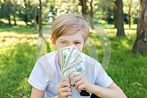 A boy in the park covered his face with dollar bills and looks menacingly ahead