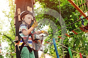 Boy passing the cable route high among trees. Climbing the rope park. Summer camp