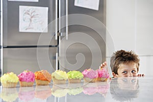 Boy Peaking Over Counter At Row Of Cupcakes photo