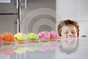 Boy Peaking Over Counter At Row Of Cupcakes photo