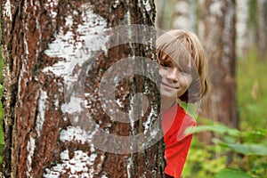 Boy peeking out from behind a tree trunk