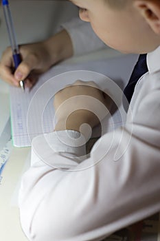 Boy with pencil writing english words by hand on traditional white notepad paper.