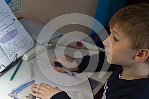 Boy with pencil writing english words by hand on traditional white notepad paper.