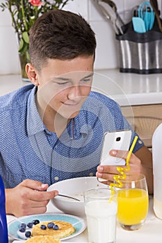 Boy with phone having breakfast in kitchen