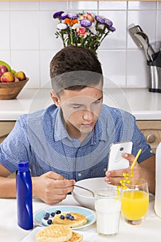 Boy with phone having breakfast in kitchen