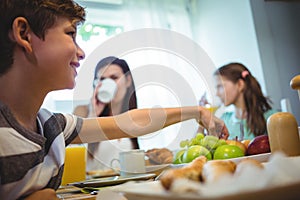 Boy picking up fruits from tray while having breakfast