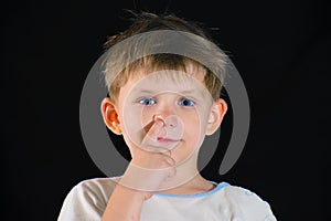 The boy picks his nose and looks at the camera, on a black background.