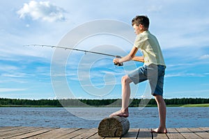 The boy on the pier, on a background of blue sky and lake, catches a fish on a bait