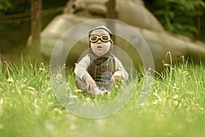 Boy in pilot helmet and glasses sitting in green grass