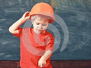 Boy play as builder or architect. Kid boy in orange hard hat or helmet, chalkboard on background. Child dreaming about