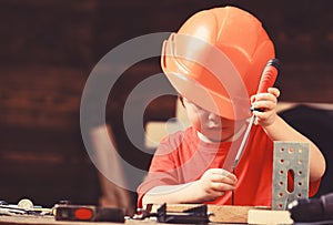 Boy play as builder or repairer, work with tools. Childhood concept. Kid boy in orange hard hat or helmet, study room