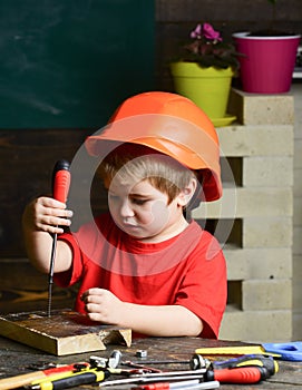 Boy play as builder or repairer, work with tools. Kid boy in orange hard hat or helmet, study room background. Childhood