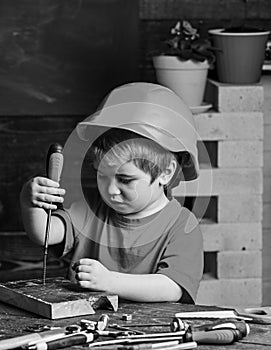 Boy play as builder or repairer, work with tools. Kid boy in orange hard hat or helmet, study room background. Childhood