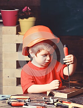 Boy play as builder or repairer, work with tools. Kid boy in orange hard hat or helmet, study room background. Childhood