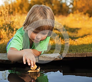 boy play with autumn leaf ship in water