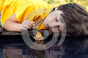 Boy play with autumn leaf ship in water,