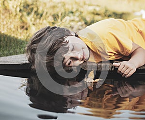 Boy play with autumn leaf ship in water, children in park play with leaf in river