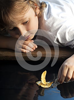 boy play with autumn leaf ship in water, children in park play with leaf in river