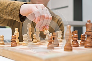 Boy play chess sitting at table closeup. Hand of child move white pawn on wooden chessboard. Game strategy, tactics.
