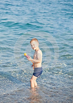 Boy play with water gun and having fun in sea or ocean waves in a summer sunny day. Ocean coast and beach. Active lifestyle and