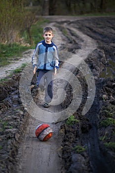 Boy playing with a ball on the mud road