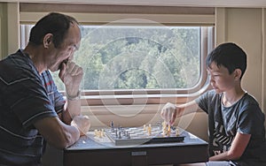 Boy playing chess with his grandfather at train.