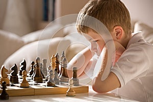 Boy playing chess in the room. Little clever boy concentrated and thinking while playing chess at home