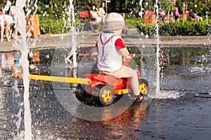 A boy is playing in the city fountain at hot weather