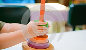 Boy is playing with colorful wooden rainboy toy pyramid.