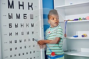 Boy playing doctor with oculist sign board and pointer.