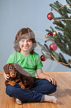 Boy playing with dog near the Christmas fir-tree