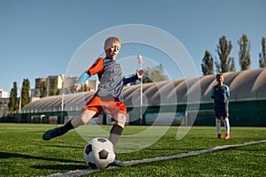 Boy playing football on field and kicking soccer ball