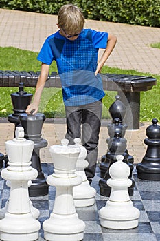 Boy playing giant chess outdoors in park. Child thinking strategically about his next move.