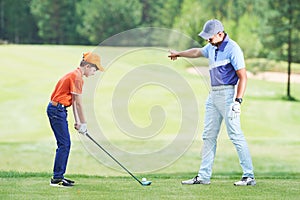 Boy playing golf in summer with trainer