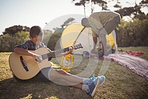 Boy playing guitar while father setting up a tent in background