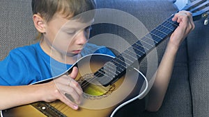 Boy is playing guitar sitting on the couch. Concept of learning to play a musical instrument.