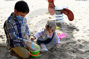 Boy playing with his little sister in a playground, they play filling a bucket of sand