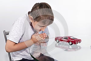 Boy playing with red sports car on a glass table
