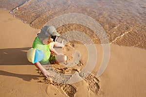 Boy playing with sand and water on a tropical beach, dressed in protective wetsuit, wearing armbands